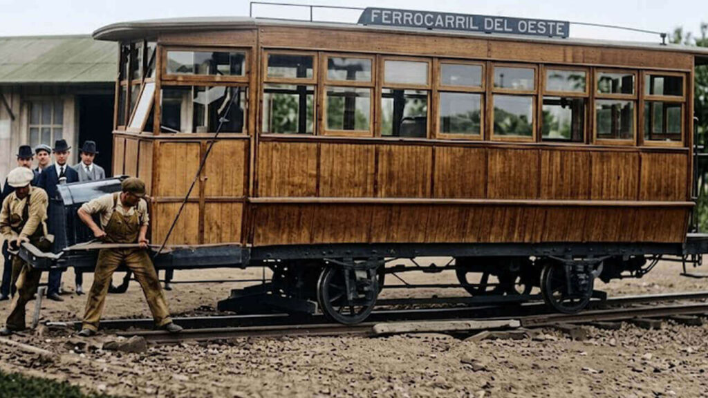 El mismo tranvía, y la misma foto, pero llevada a color. Dos jóvenes trabajadores giran uno de los tres tranvías en la Estación de Ituzaingó sobre una rueda mecánica.