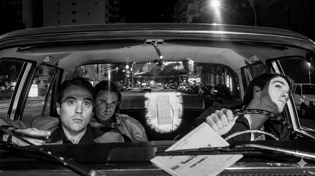 Los tres protagonistas de la película 76 89 03 viajando en auto en blanco y negro