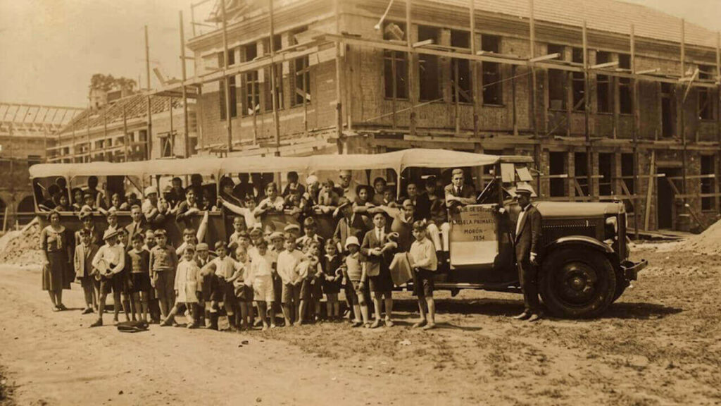 Fotaza de alumnos de Escuela Primera subiendo al transporte escolar y de fondo el Colegio Ward en construcción