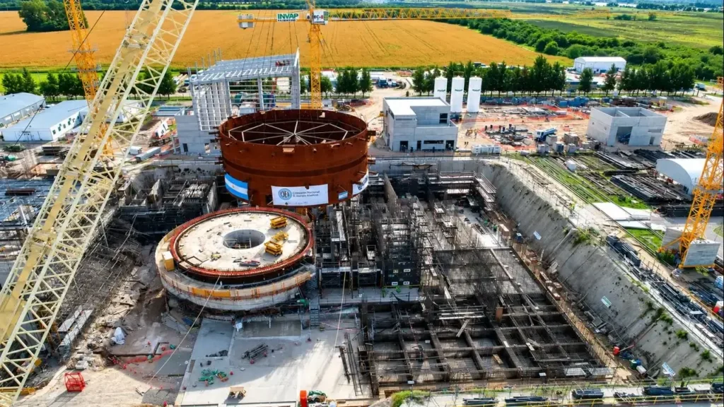 Montaje de los grandes módulos de acero del edificio de contención, que muestra la complejidad de la ingeniería. Más una vista cenital del pozo de construcción, donde se observan las grúas, la estructura circular y el avance de la obra civil. Es una fotografía cercana de la estructura del reactor, ideal para explicar el funcionamiento del CAREM y la magnitud de sus componentes.
Vista cenital del pozo de construcción, donde se observan las grúas, la estructura circular y el avance de la obra civil.