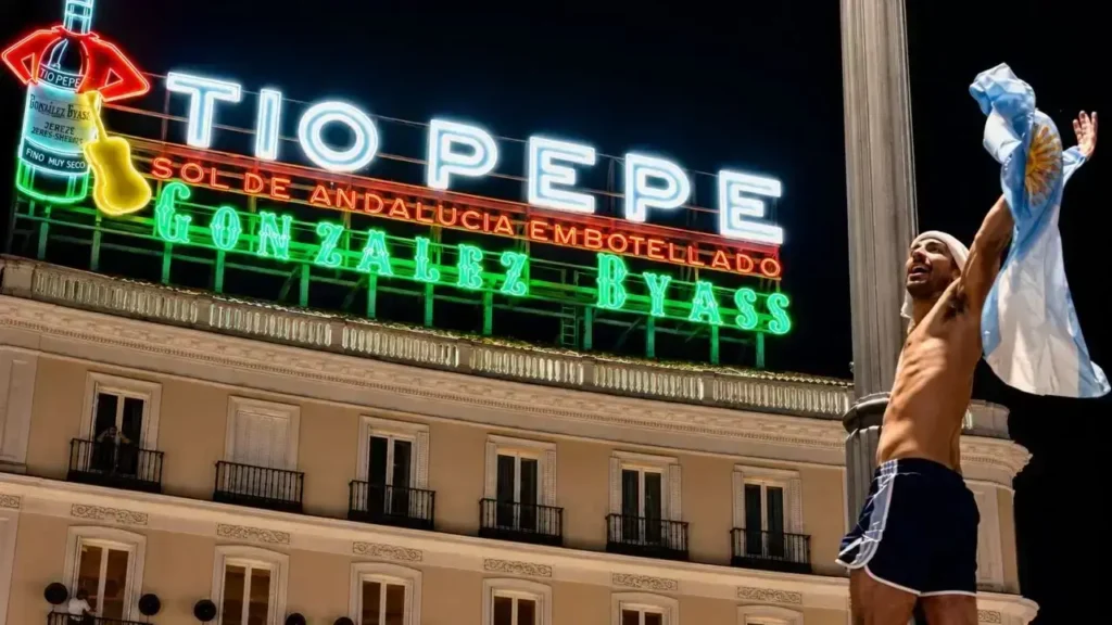 Esta imagen también fue tomada en la Puerta del Sol, en el centro de Madrid.

Lo que aparece al fondo es el famoso cartel luminoso de Tío Pepe, uno de los símbolos más reconocibles de la ciudad. El edificio sobre el que está instalado corresponde al número 1 de la Puerta del Sol, y el cartel domina la plaza desde hace décadas (con un breve período en el que fue retirado antes de volver a colocarse).