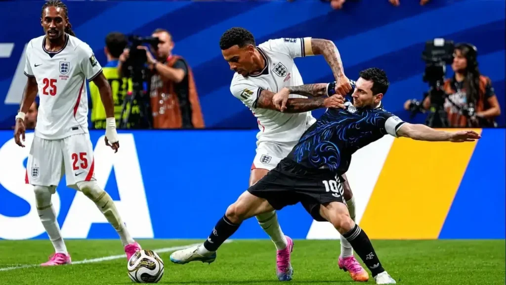 Lionel Messi protege el balón ante la fuerte marca de Reece James, que intenta frenar su avance con un forcejeo cuerpo a cuerpo. A la izquierda observa la jugada Marc Guéhi (25), en una de las acciones de mayor fricción de la semifinal entre la Selección Argentina e Inglaterra.