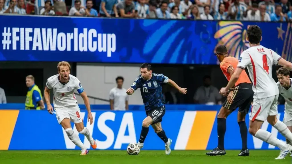 Lionel Messi conduce la pelota y acelera el ataque de la Selección Argentina mientras Harry Kane (9) sigue la jugada desde la izquierda y Reece James (4) se prepara para cerrar los espacios. La acción se desarrolla bajo la atenta mirada del árbitro durante la semifinal del Mundial 2026 frente a Inglaterra.