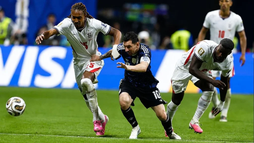 Lionel Messi lucha por la posesión de la pelota ante la marca de John Stones (5), mientras Reece James (24) y Jude Bellingham (10) siguen de cerca la acción. El capitán de la Selección Argentina enfrenta la presión inglesa en una de las jugadas más intensas de la semifinal del Mundial 2026.