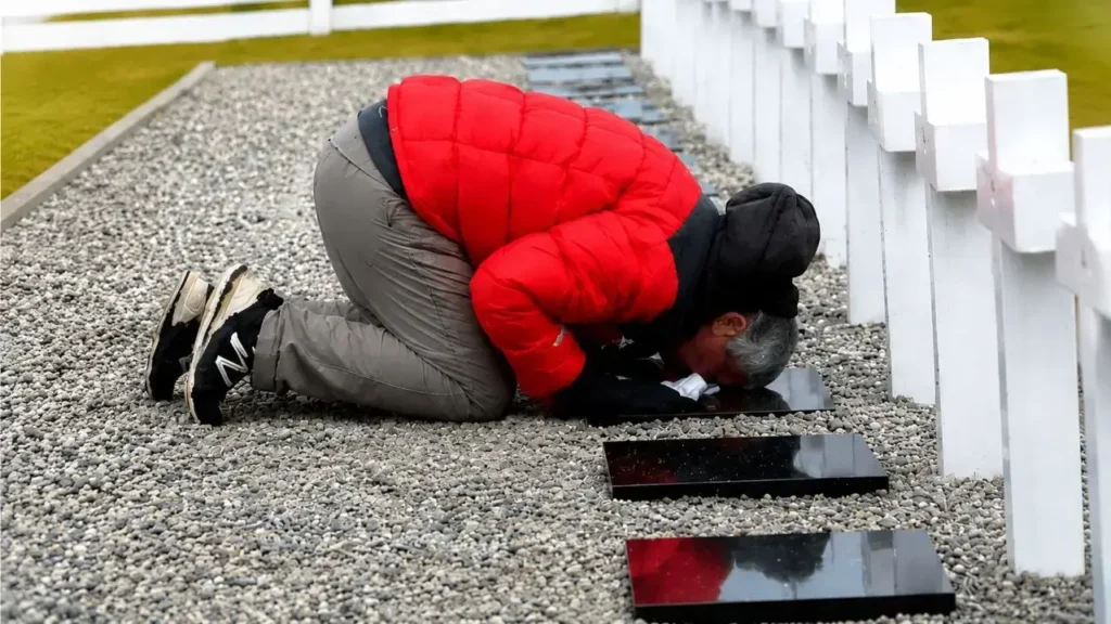Eduardo Canitrot se arrodilla sobre las tierras de Darwin, donde se encuentra el Cementerio Argentino de los caídos en la guerra.