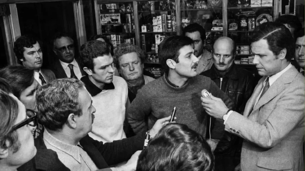 Esta es la imagen original,en blanco y negro, si aplicar una cura mediante IA de color. Mariano Pujadas y sus diechiocho compañeros habla con el periodista Daniel Carreras.
