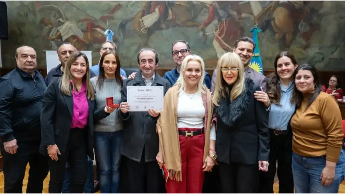 La Democracia distingue al Fraude. En la foto: Pío Antonio Cappellano: ubicado en el centro, sosteniendo el diploma de distinción que lleva su nombre. Alejandra Liquitay (concejala de Morón, Juntos por el Cambio / La Libertad Avanza): A la derecha inmediata del homenajeado (pantalón rojo y chal beige). Vanina Moro (concejala de Morón, Unión por la Patria): A la izquierda inmediata de Cappellano (suéter gris, sosteniendo la caja de la medalla). Daniela Burgos: En el extremo derecho (remera mostaza/marrón). Silvina Valdevenito (concejala): a la izquierda de Vanina Moro (camisa fucsia y saco negro). Analía Zapulla (exconcejala/referente local de JxC): a la derecha de Alejandra Liquitay (de saco negro con cuello de piel y lentes). Leandro Ugartemendia (concejal de Juntos por el Cambio): Detrás de Zapulla y Liquitay. Marcelo González (concejal): Detrás, entre Vanina Moro y Cappellano (con anteojos). Claudio Faro: al fondo a la izquierda (con campera deportiva oscura / chomba).