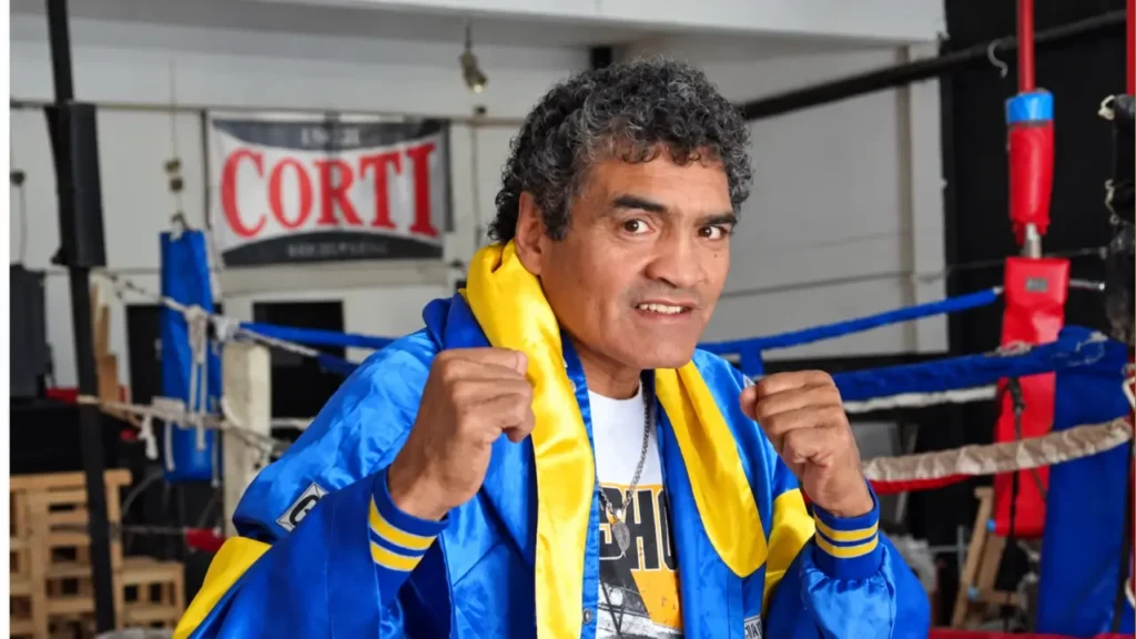 Con una campera azul y amarilla y los puños en alto, Castro posa junto al ring, rodeado de elementos de entrenamiento. Su imagen quedó asociada a una carrera de resistencia y grandes regresos, entre ellos la victoria por nocaut ante John David Jackson en una de las peleas más emblemáticas de su trayectoria.
